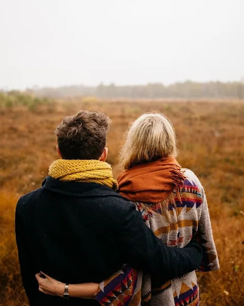 A couple in coats standing in an open field.
