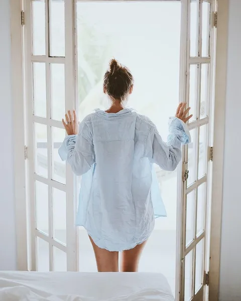 A woman in a sheer white shirt seen from behind by a window.