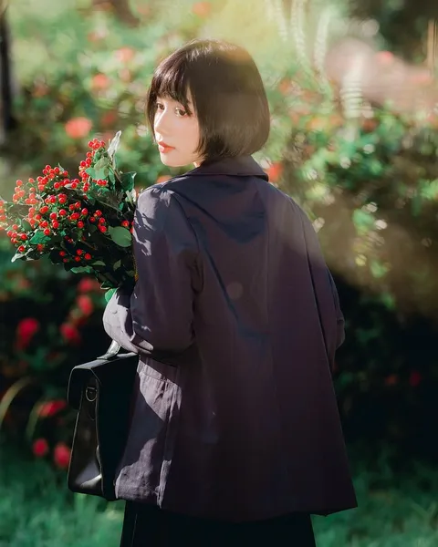 A woman in a grey coat holding a camera on a wet street.