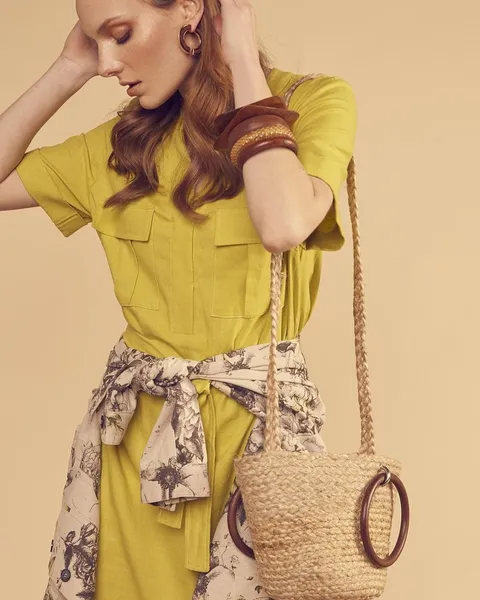 A woman in a chartreuse top with a printed skirt and a straw bag.