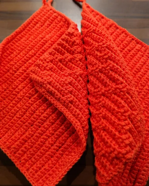 A red cable-knit garment folded flat on a pale surface.