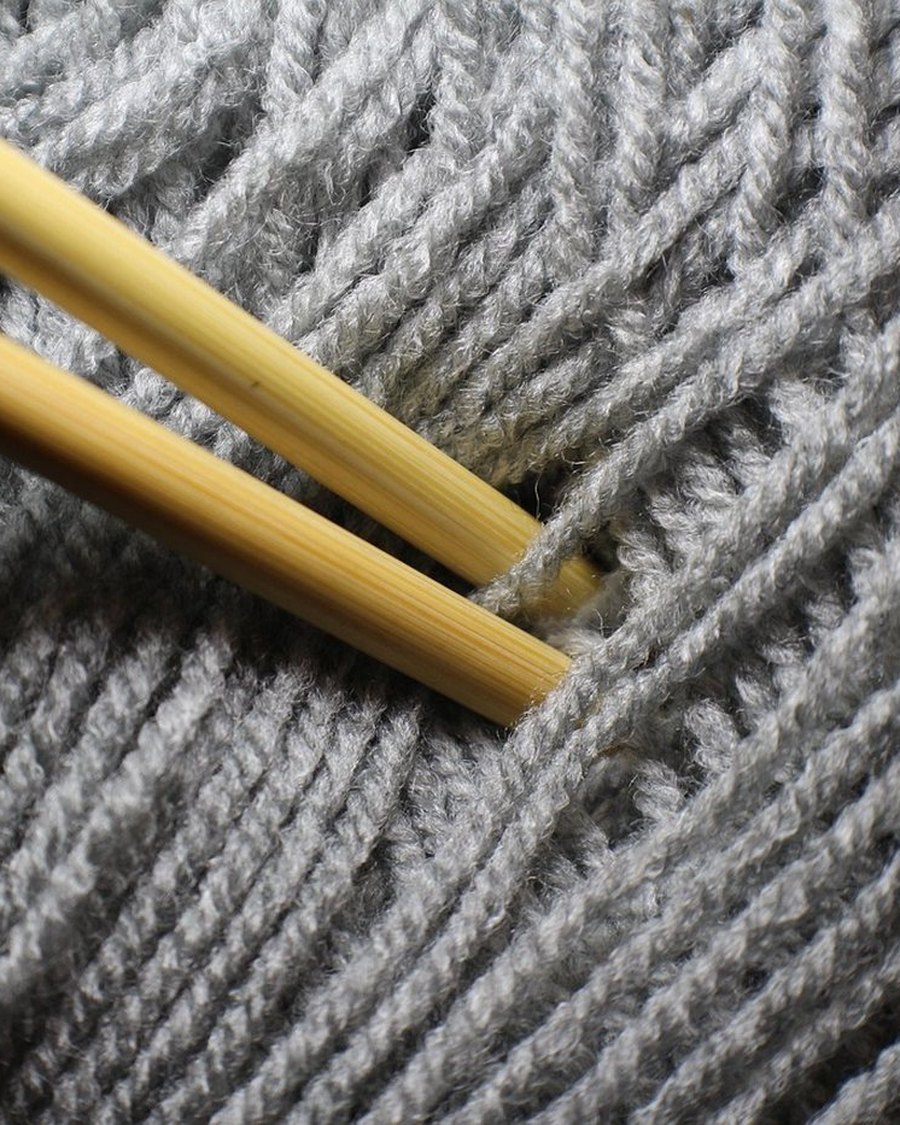 A steel knitting needle resting on grey knit fabric.