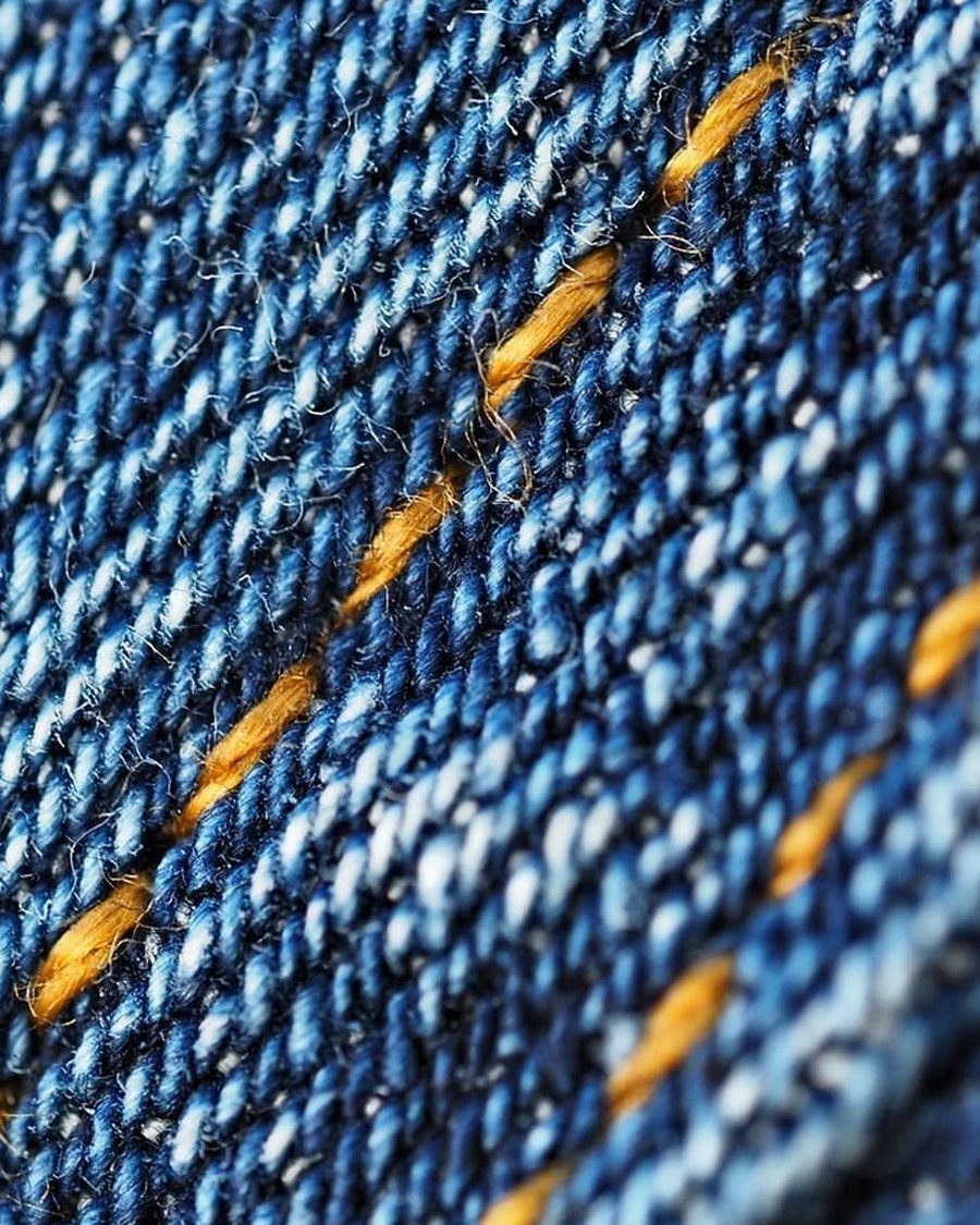 A close-up of indigo denim with orange stitching.