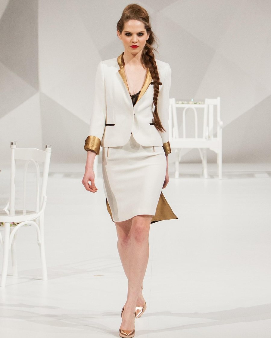 A woman in a white blazer suit standing against a pale wall.