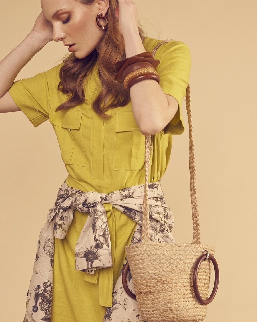 A woman in a chartreuse top with a printed skirt and a straw bag.